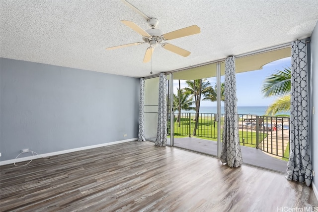 unfurnished room featuring a wall of windows, hardwood / wood-style flooring, ceiling fan, a water view, and a textured ceiling