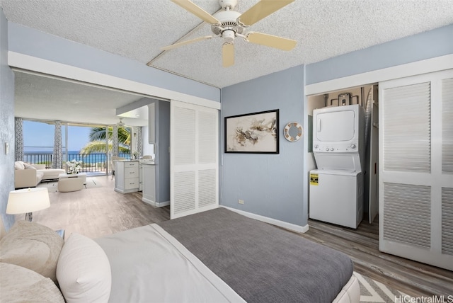 bedroom featuring stacked washer / drying machine, hardwood / wood-style floors, a textured ceiling, and ceiling fan