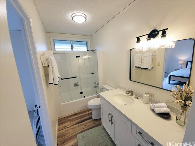 full bathroom featuring hardwood / wood-style flooring, bath / shower combo with glass door, vanity, a textured ceiling, and toilet