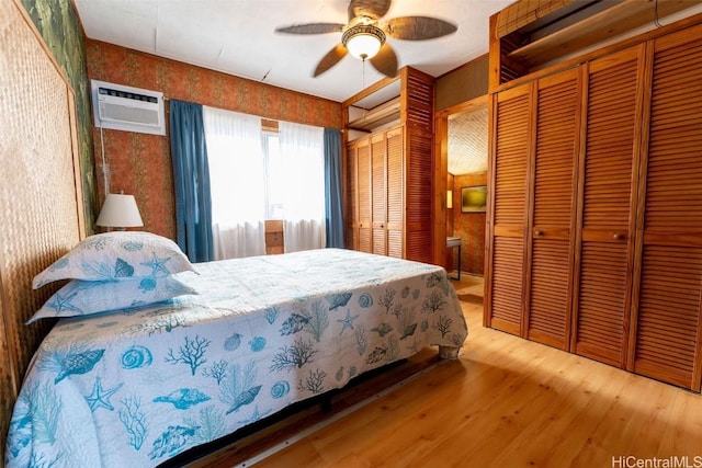 bedroom with a wall mounted air conditioner, two closets, a ceiling fan, wood finished floors, and wallpapered walls