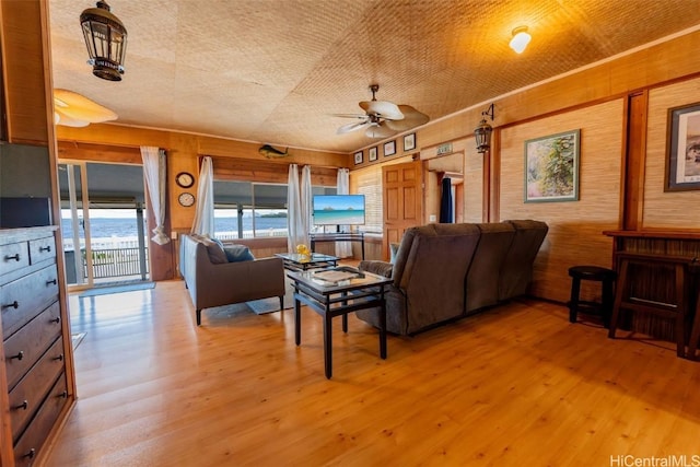 living area featuring wooden walls, light wood-type flooring, and ceiling fan