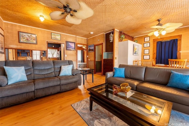 living area featuring ornamental molding, wood walls, ceiling fan, and wood finished floors