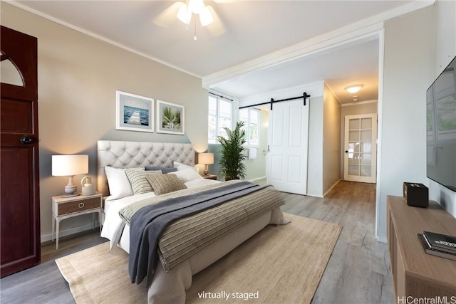 bedroom with a barn door, baseboards, light wood finished floors, and ornamental molding