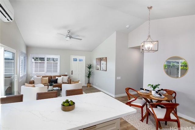 kitchen with hanging light fixtures, light hardwood / wood-style floors, ceiling fan with notable chandelier, vaulted ceiling, and an AC wall unit