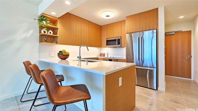 kitchen with sink, appliances with stainless steel finishes, a kitchen breakfast bar, tasteful backsplash, and kitchen peninsula