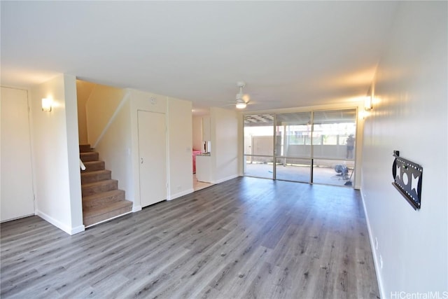 unfurnished living room featuring ceiling fan, stairway, baseboards, and wood finished floors