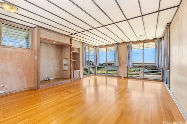 unfurnished room with hardwood / wood-style floors, a wall of windows, and built in shelves