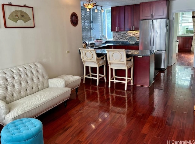 kitchen with sink, stainless steel refrigerator, a breakfast bar, backsplash, and dark hardwood / wood-style flooring