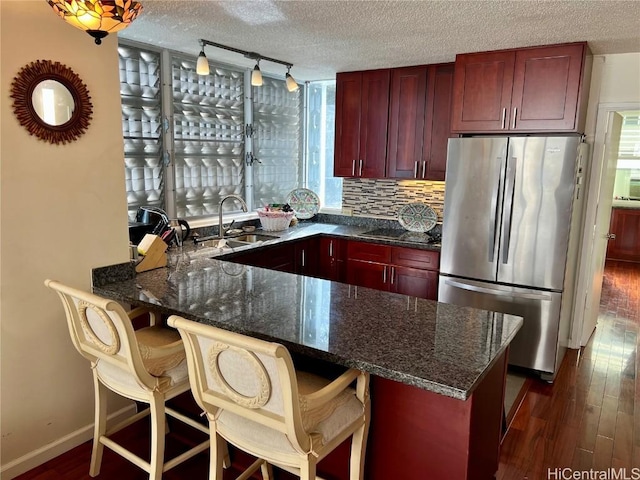 kitchen featuring dark hardwood / wood-style floors, sink, stainless steel fridge, kitchen peninsula, and a textured ceiling