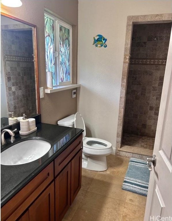 bathroom with tiled shower, vanity, toilet, and tile patterned flooring