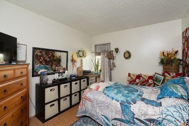 bedroom featuring light hardwood / wood-style flooring, an AC wall unit, and a textured ceiling