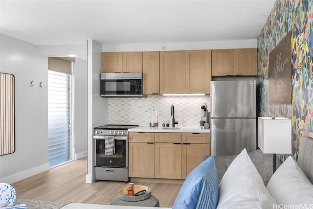 kitchen featuring sink, tasteful backsplash, light brown cabinets, light wood-type flooring, and appliances with stainless steel finishes