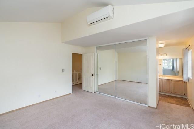 unfurnished bedroom with vaulted ceiling, an AC wall unit, ensuite bathroom, light carpet, and a closet