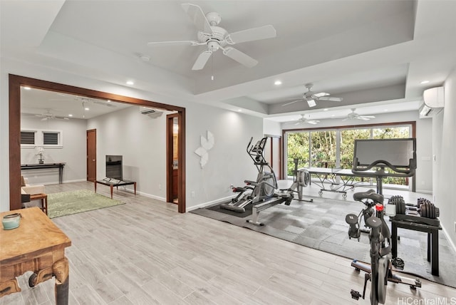 workout room featuring a wall unit AC, light wood-type flooring, and a tray ceiling