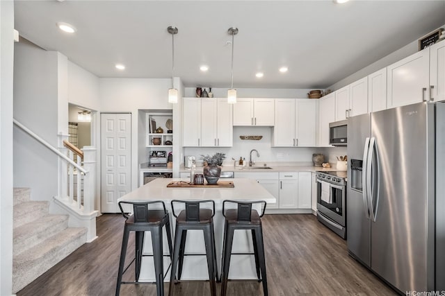 kitchen with a kitchen breakfast bar, light countertops, white cabinets, stainless steel appliances, and a sink