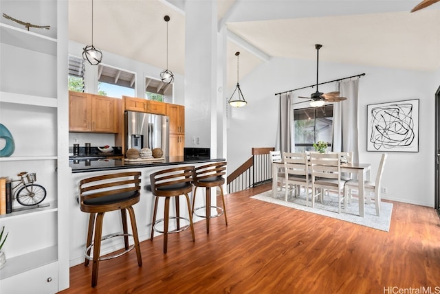 kitchen with a breakfast bar area, wood finished floors, dark countertops, and stainless steel fridge with ice dispenser