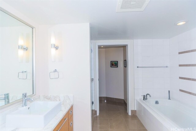 bathroom with a relaxing tiled tub, vanity, and tile patterned floors