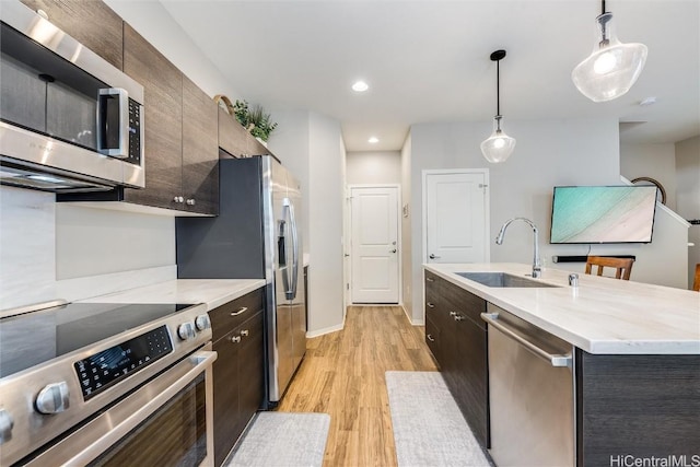 kitchen featuring sink, light hardwood / wood-style flooring, a kitchen island with sink, stainless steel appliances, and decorative light fixtures