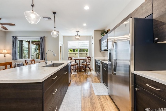 kitchen featuring sink, decorative light fixtures, light wood-type flooring, appliances with stainless steel finishes, and an island with sink