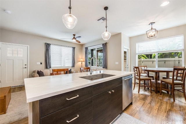 kitchen with dark brown cabinetry, sink, decorative light fixtures, and an island with sink