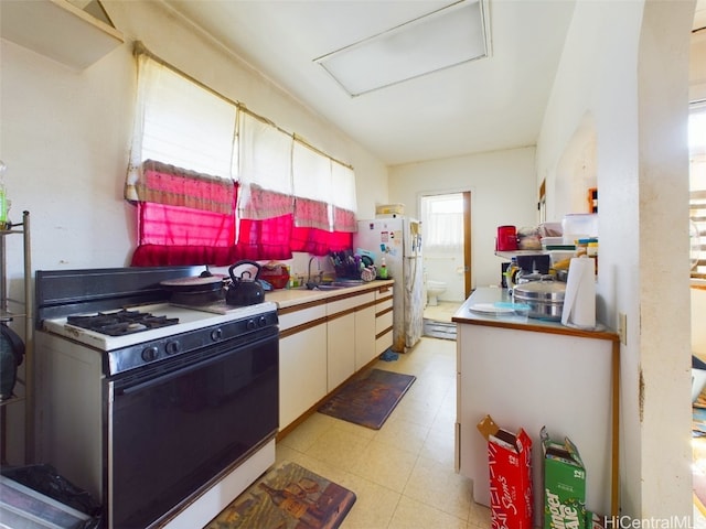 kitchen featuring white cabinetry, white gas range, sink, and refrigerator