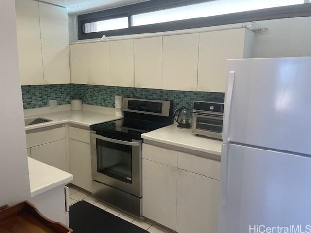 kitchen featuring white cabinets, backsplash, stainless steel range with electric stovetop, white refrigerator, and light tile patterned floors