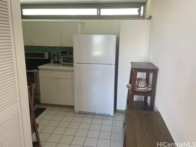 kitchen with stainless steel range with electric stovetop, white refrigerator, light tile patterned flooring, decorative backsplash, and cream cabinetry