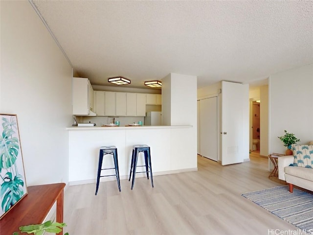 kitchen featuring white cabinetry, light wood-type flooring, white fridge, kitchen peninsula, and a textured ceiling