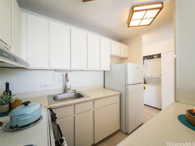 kitchen with sink, white cabinets, stacked washer and dryer, white appliances, and a textured ceiling