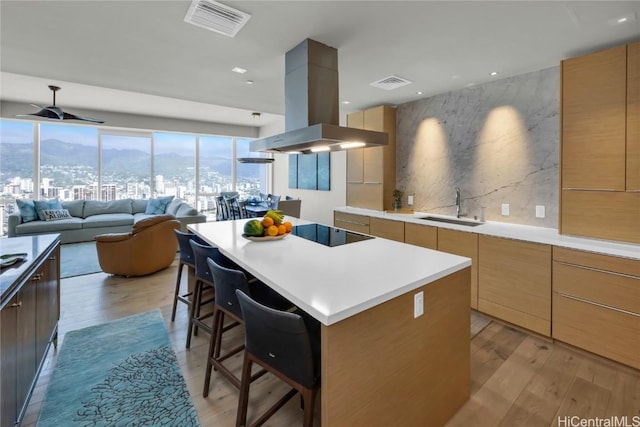 kitchen with island exhaust hood, light countertops, open floor plan, a kitchen island, and a sink