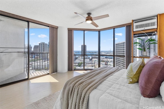 bedroom featuring an AC wall unit, access to outside, light hardwood / wood-style floors, floor to ceiling windows, and a water view