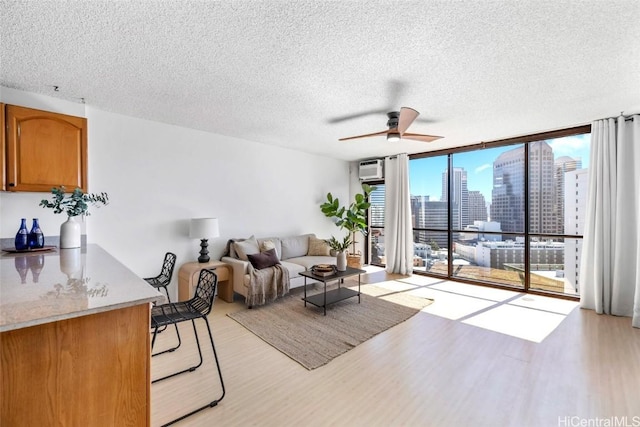 living room featuring a textured ceiling, light hardwood / wood-style flooring, expansive windows, and ceiling fan