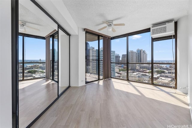 spare room featuring a wall mounted AC, expansive windows, ceiling fan, a textured ceiling, and light hardwood / wood-style flooring