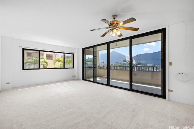 empty room with expansive windows, a mountain view, light colored carpet, and ceiling fan