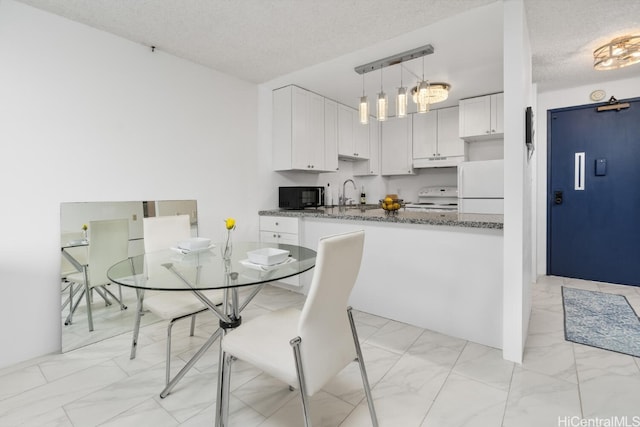 kitchen featuring pendant lighting, dark stone countertops, white cabinets, white appliances, and a textured ceiling