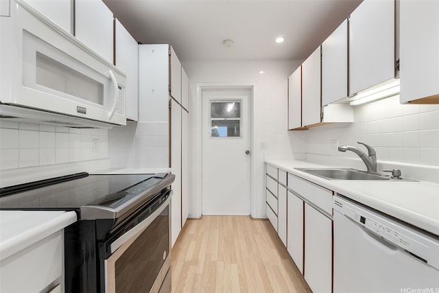kitchen featuring light wood-style flooring, a sink, light countertops, white appliances, and backsplash