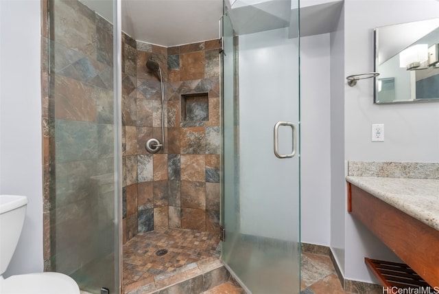 bathroom featuring vanity, a shower stall, stone finish floor, and toilet