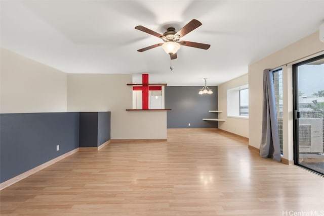 empty room with ceiling fan with notable chandelier, light wood-type flooring, and baseboards