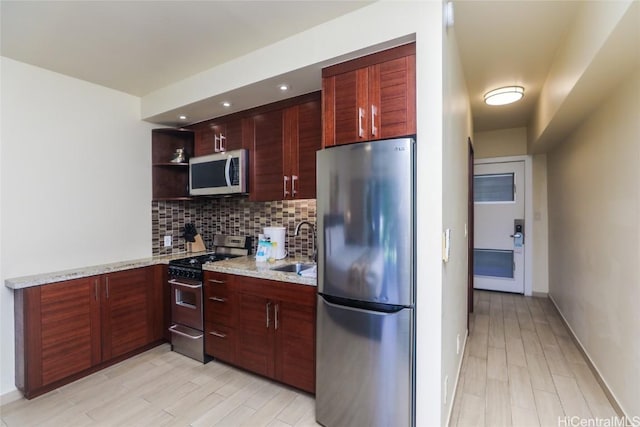 kitchen featuring sink, backsplash, stainless steel appliances, light stone countertops, and light hardwood / wood-style flooring