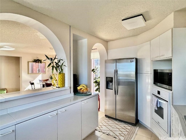 kitchen featuring a textured ceiling, stainless steel appliances, white cabinets, and light tile patterned flooring