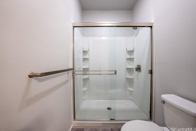 bathroom featuring wood-type flooring, a shower with shower door, and toilet