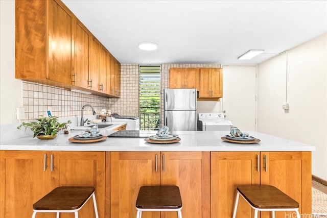 kitchen featuring washer / dryer, freestanding refrigerator, a sink, light countertops, and backsplash