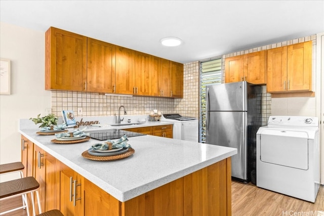 kitchen with brown cabinetry, freestanding refrigerator, a sink, washer / dryer, and a peninsula