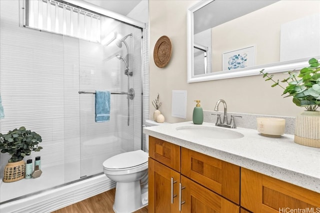 bathroom featuring wood finished floors, a stall shower, vanity, and toilet