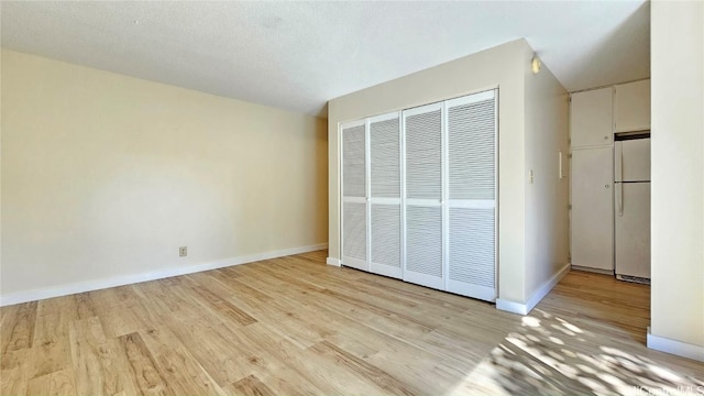 unfurnished bedroom featuring light wood-style flooring, a closet, freestanding refrigerator, and baseboards