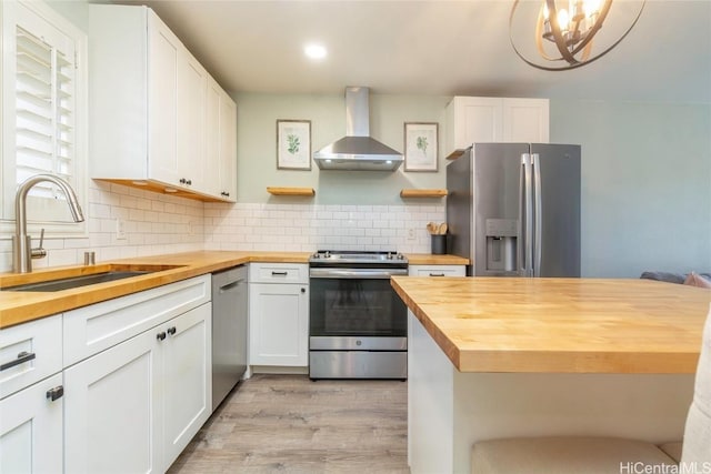 kitchen featuring appliances with stainless steel finishes, wood counters, sink, and wall chimney range hood