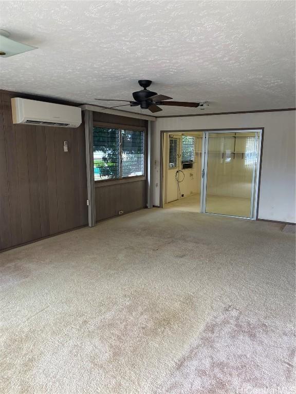 carpeted spare room with ceiling fan, wooden walls, a textured ceiling, and an AC wall unit