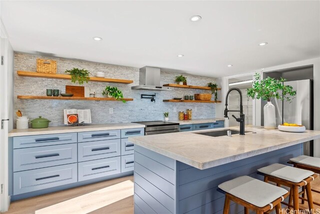 kitchen featuring electric stove, open shelves, a kitchen island with sink, wall chimney range hood, and a kitchen breakfast bar