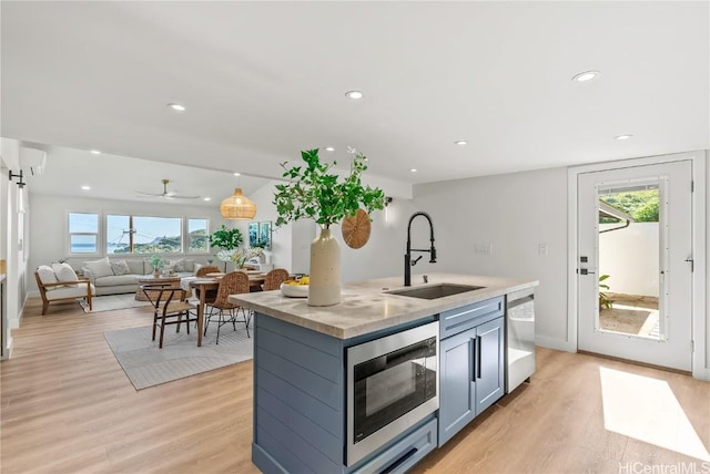 kitchen featuring a center island with sink, light countertops, a sink, built in microwave, and dishwasher