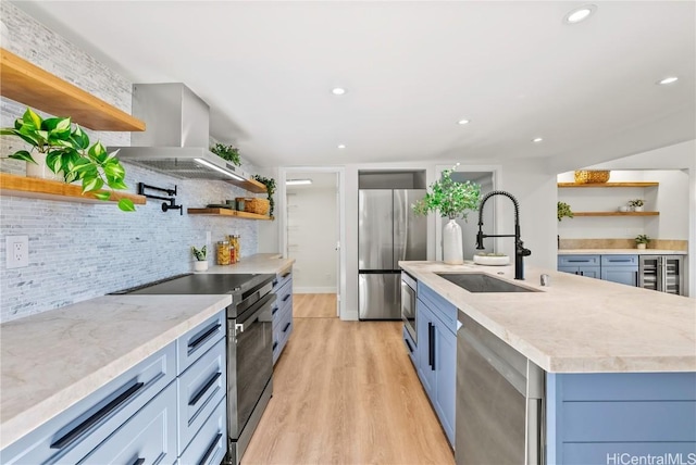 kitchen featuring stainless steel appliances, light countertops, range hood, open shelves, and a center island with sink